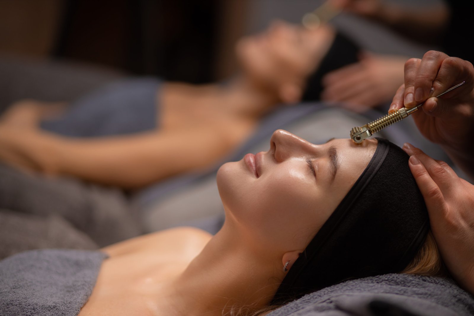 close-up photo of woman getting massage on forehead with the use of jade or mesotherapy roller by professional masseur or cosmetologist, woman enjoy procedure, lie with closed eyes